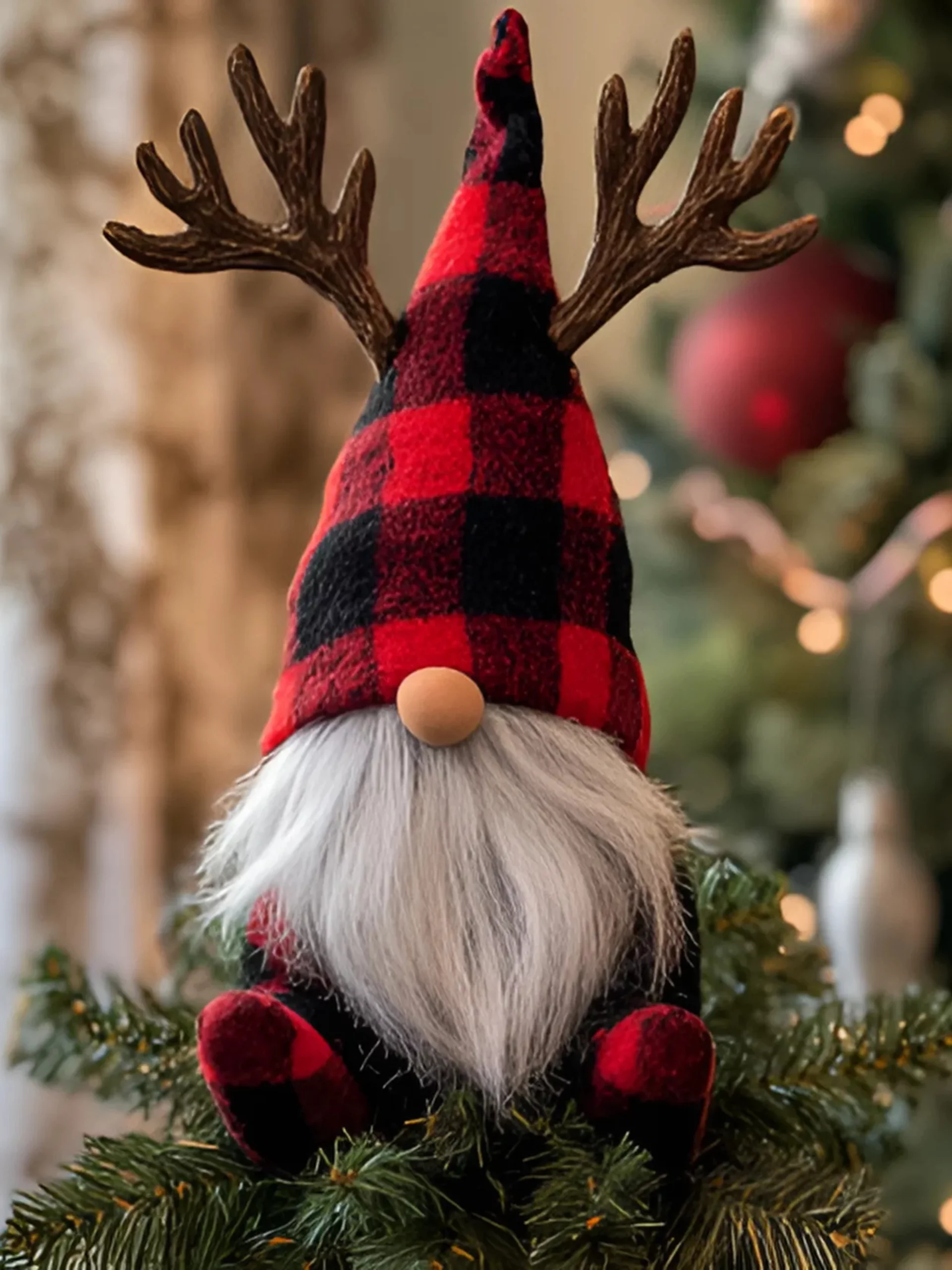 Festive Christmas gnome dressed in red and black buffalo plaid with reindeer antlers, a fluffy white beard, and a wooden nose, sitting atop a Christmas tree with twinkling lights in the background.