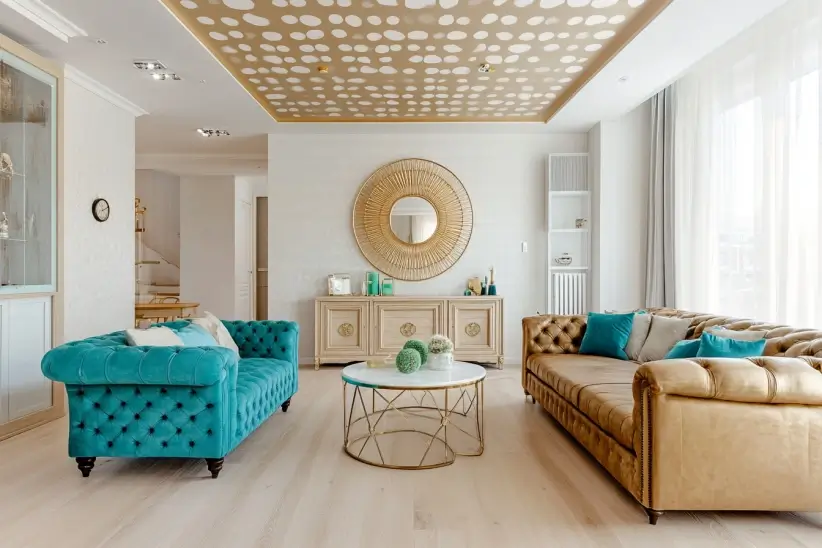Elegant living room with a gold polka-dot ceiling, turquoise and tan velvet sofas, and sunburst mirror above a wooden console table.