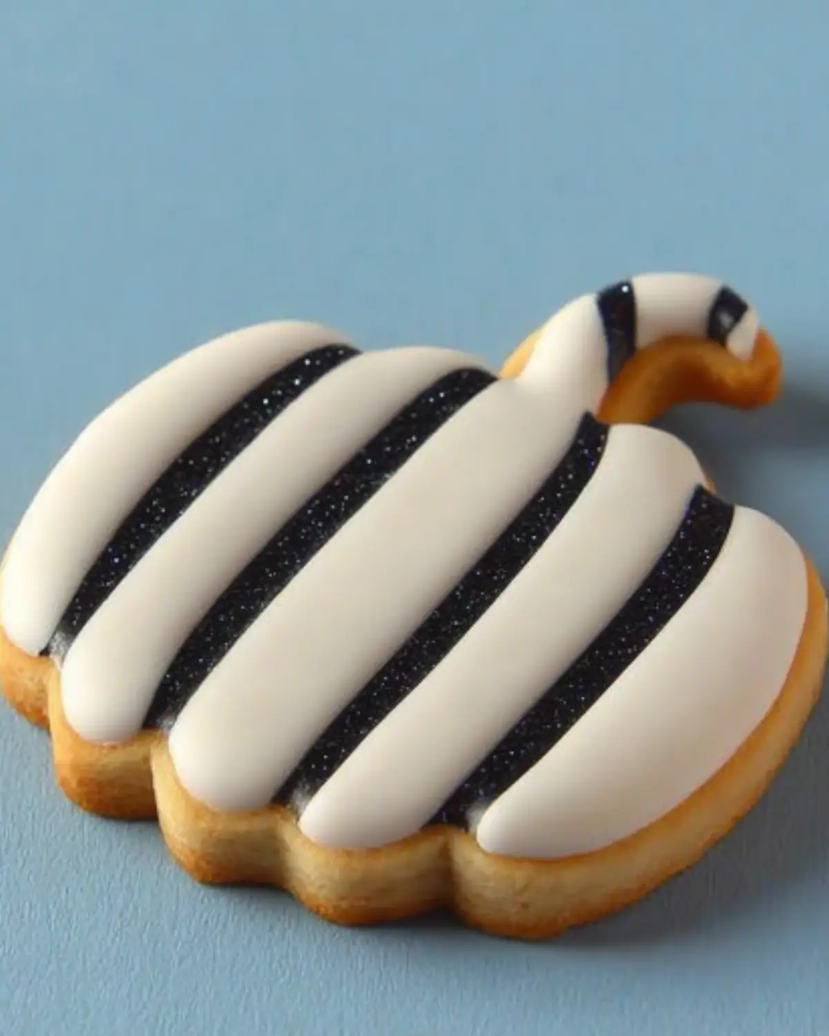Pumpkin-shaped sugar cookie decorated with black and white striped royal icing