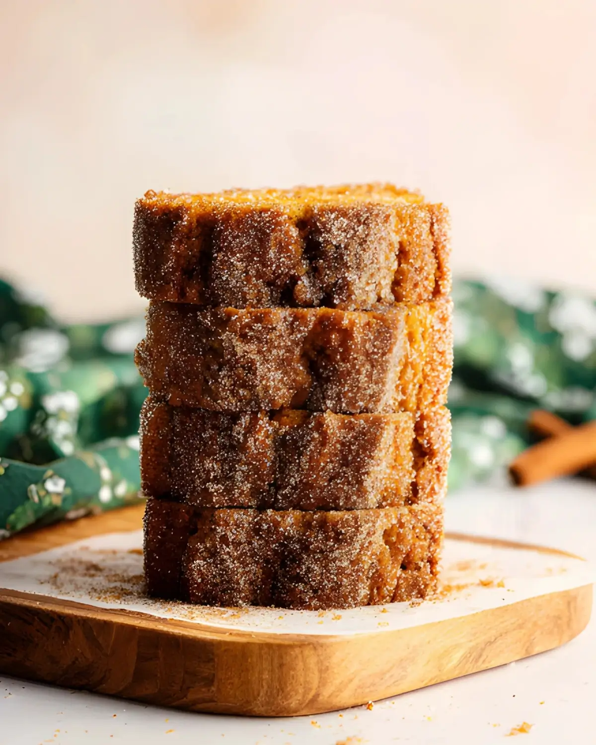 Stack of pumpkin bread slices coated in cinnamon sugar on a wooden board with a festive green background