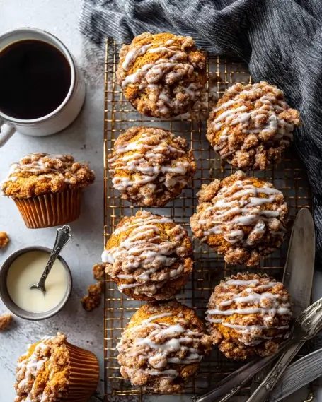 Pumpkin streusel muffins drizzled with white glaze on a cooling rack, served with coffee and cream.