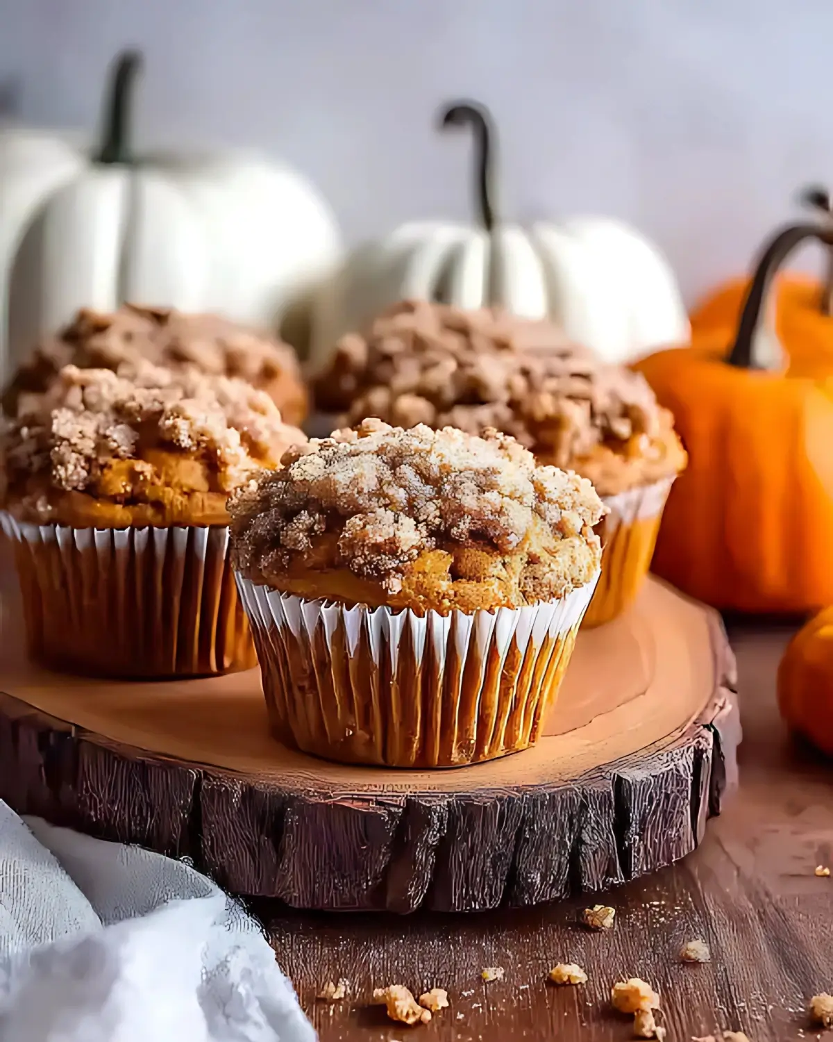 Pumpkin streusel muffins on a wooden board, topped with crumbly cinnamon sugar and surrounded by pumpkins.