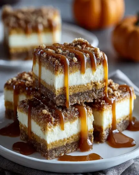 Layered Pumpkin Cheesecake Bars with Streusel and Caramel Pumpkin cheesecake bars stacked on a plate with graham cracker crust, creamy cheesecake, pumpkin spice layer, streusel topping, and caramel drizzle.