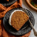 Pumpkin bundt cake slice with white glaze served on a black plate with fork