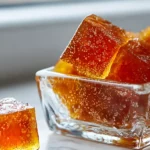 Golden gelatin cubes with bubbles in a clear glass dish on a marble surface