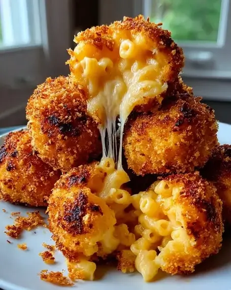 Golden air fryer mac and cheese balls stacked on a plate, with melted cheese stretching from the center for a gooey, crispy bite.