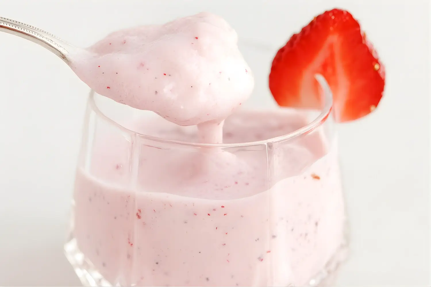 Creamy strawberry mousse in a glass with a spoonful lifted and a fresh strawberry slice on the rim