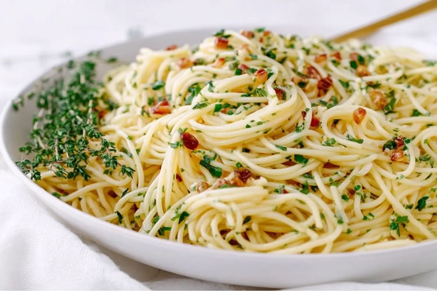Bowl of spaghetti tossed with garlic, herbs, and olive oil, garnished with parsley and thyme.