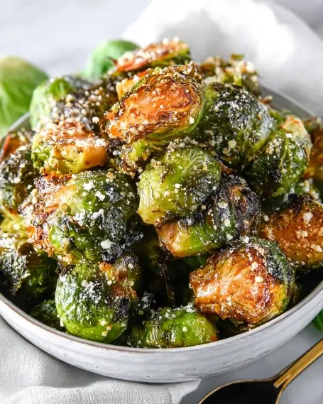 Crispy roasted Brussels sprouts in a white bowl, sprinkled with parmesan cheese and sea salt.