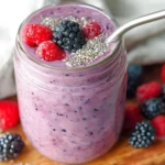 Creamy mixed berry smoothie in a mason jar topped with chia seeds, raspberries, and a blackberry, with a metal straw.
