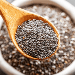 Wooden spoon filled with dry chia seeds held above a bowl full of chia seeds.