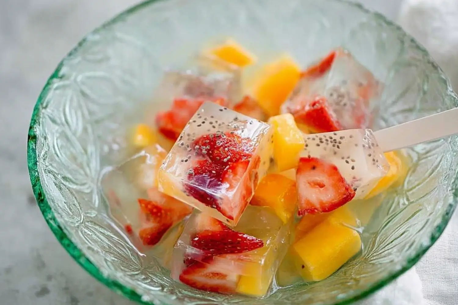 "Colorful fruit kanten jelly cubes with strawberries and mango served in a green glass bowl"