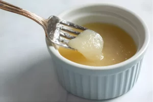 Fork lifting unflavored gelatin from a ramekin, showcasing its smooth texture and gel-like consistency.