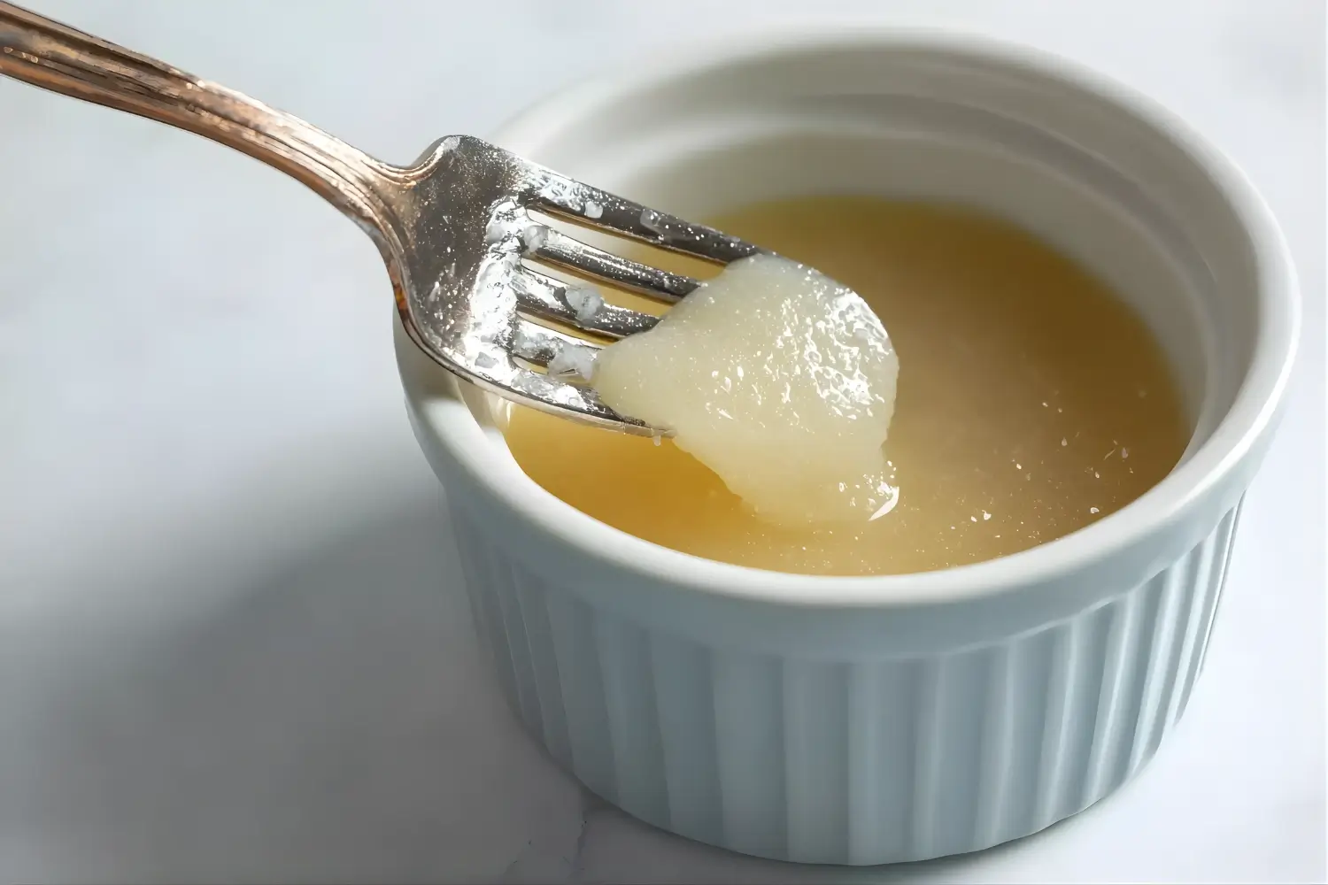 Fork lifting unflavored gelatin from a ramekin, showcasing its smooth texture and gel-like consistency.