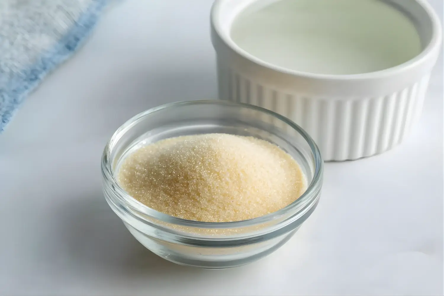 A small bowl of unflavored gelatin powder placed next to a ramekin of water.